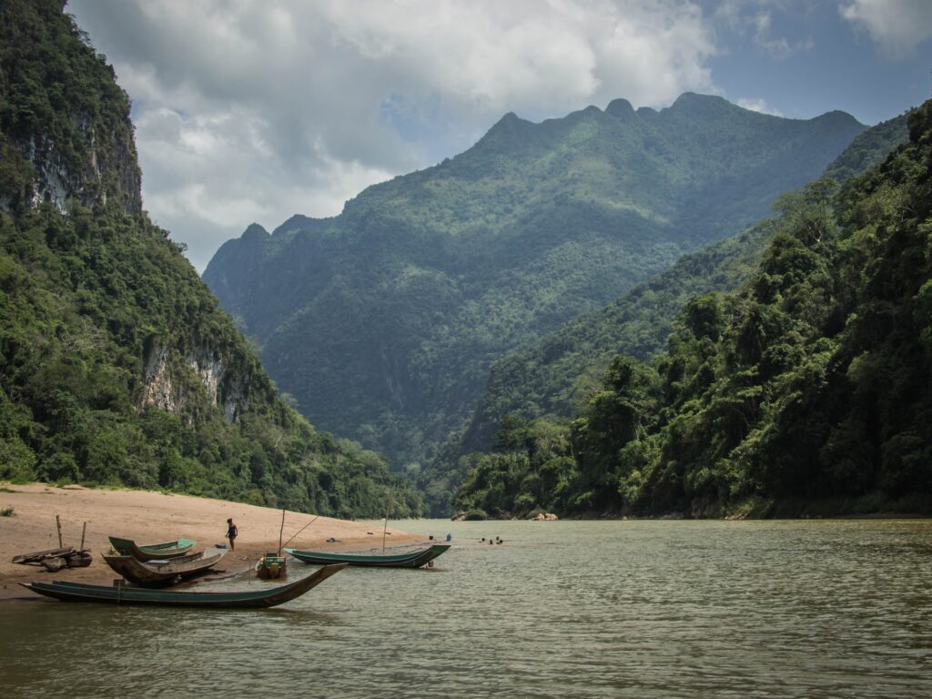 River with a tree covered mountain in the background and a small boat on the shore